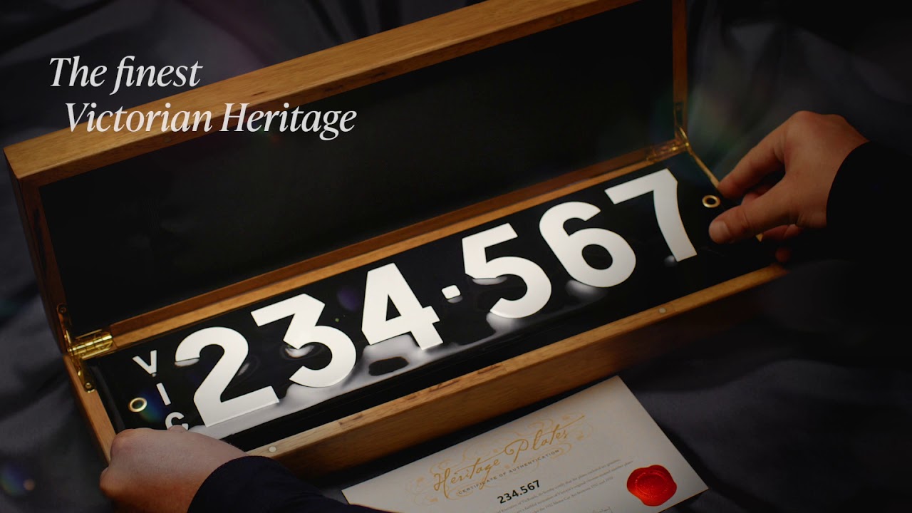 Heritage plate - white text on a flat black background, two sets of numbers separated by a small square separator (e.g. 234 - 567), with VIC vertically down the left side. Two screws, one each on the left and right edges centred vertically