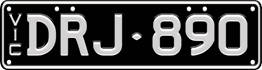 Slimline black plate - white text on a flat black background, two sets of characters separated by a small diamond separator (e.g. BTZ- 168), with VIC vertically down the left side. Four screws on the top edge of the plate